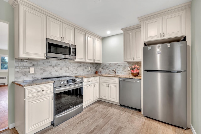 kitchen featuring appliances with stainless steel finishes, a sink, light wood-style floors, light stone countertops, and radiator heating unit