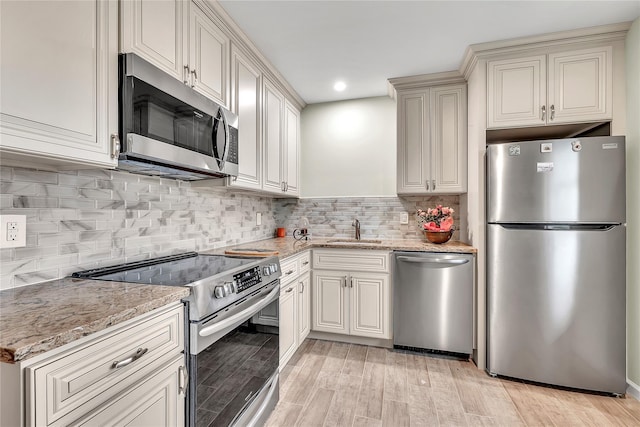 kitchen with appliances with stainless steel finishes, light stone countertops, light wood-style floors, a sink, and decorative backsplash