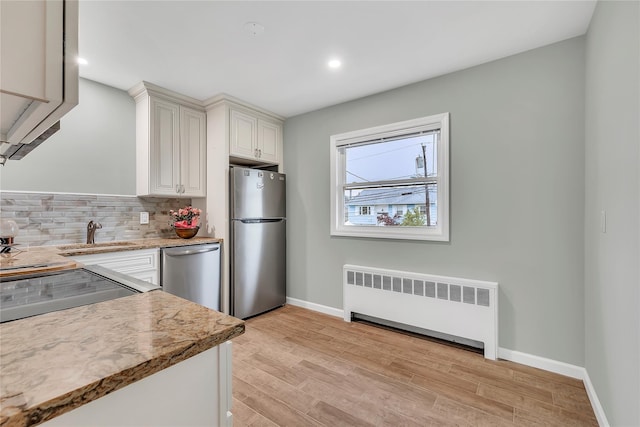 kitchen with radiator heating unit, stainless steel appliances, a sink, decorative backsplash, and baseboards