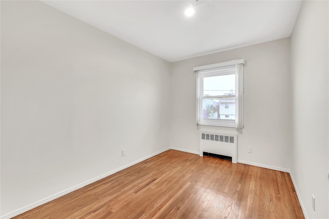 empty room featuring radiator heating unit, light wood-type flooring, and baseboards