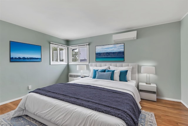 bedroom with a wall mounted AC, radiator heating unit, wood finished floors, and baseboards