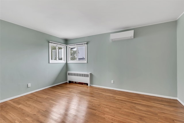 spare room with radiator heating unit, a wall unit AC, wood finished floors, and baseboards