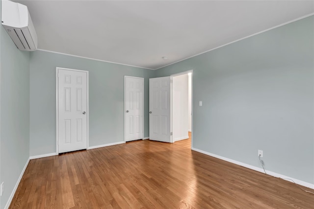 unfurnished bedroom featuring an AC wall unit, baseboards, and wood finished floors