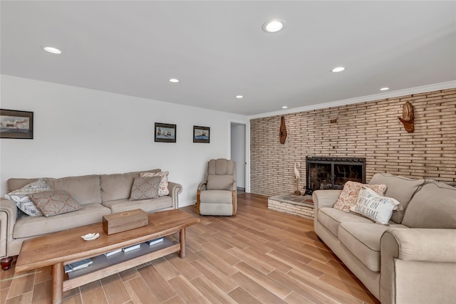 living area featuring brick wall, recessed lighting, a brick fireplace, light wood-style flooring, and baseboards