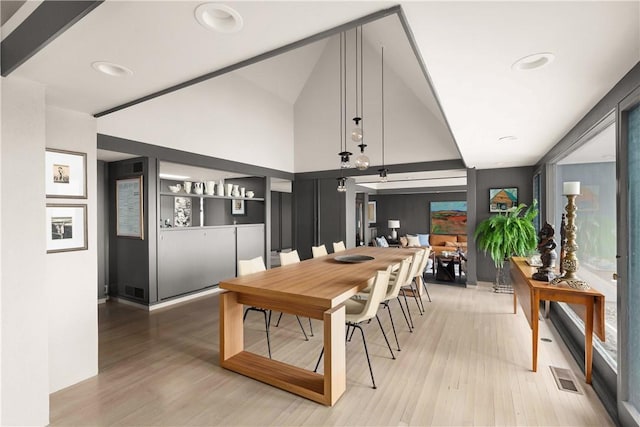 dining area featuring light wood-type flooring, high vaulted ceiling, and visible vents