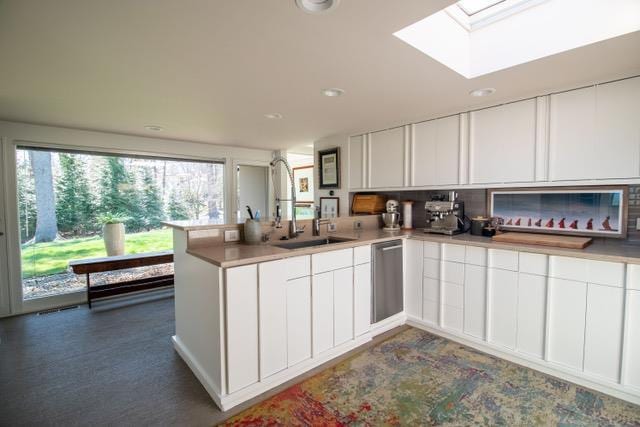kitchen with a peninsula, white cabinets, a skylight, dishwasher, and light countertops
