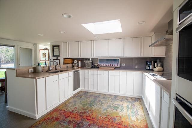 kitchen with appliances with stainless steel finishes, a sink, a peninsula, a skylight, and decorative backsplash