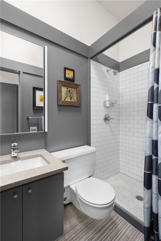 full bathroom featuring toilet, a tile shower, and vanity