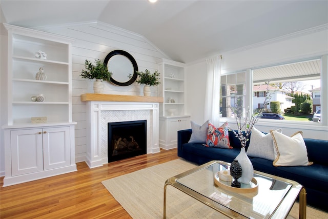 living area featuring a tiled fireplace, built in features, light wood-style flooring, and lofted ceiling