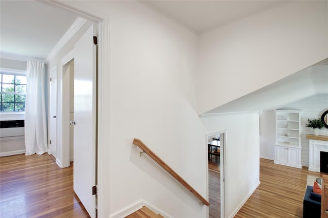corridor with light wood-style floors, baseboards, ornamental molding, and an upstairs landing