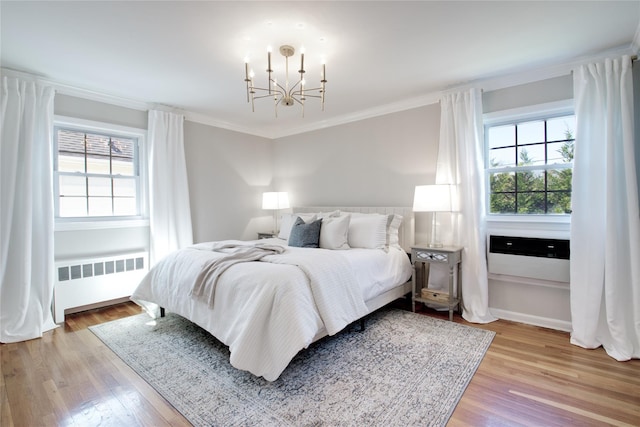 bedroom featuring a notable chandelier, baseboards, ornamental molding, radiator heating unit, and light wood-style floors
