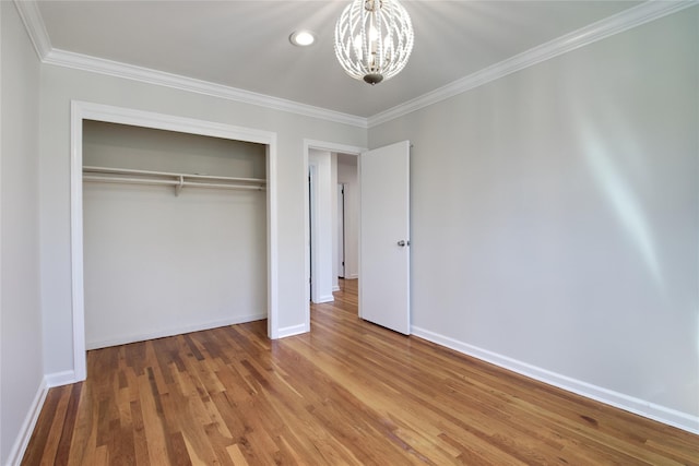 unfurnished bedroom featuring a notable chandelier, a closet, crown molding, and wood finished floors