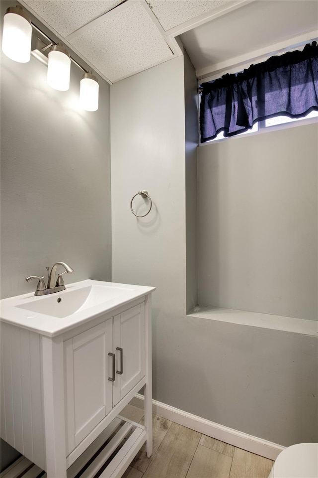 bathroom with vanity, a paneled ceiling, baseboards, toilet, and wood finished floors