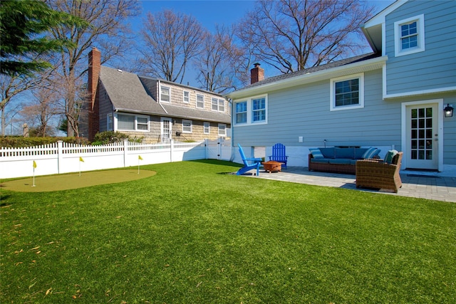 back of house featuring a chimney, an outdoor living space, a patio area, fence, and a lawn