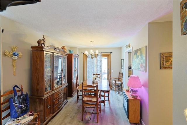 dining room with light wood-type flooring, an inviting chandelier, and a textured ceiling