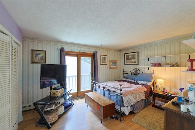 bedroom with access to exterior, wallpapered walls, wood finished floors, and a textured ceiling