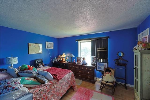 bedroom with wood finished floors, a textured ceiling, and a wall unit AC