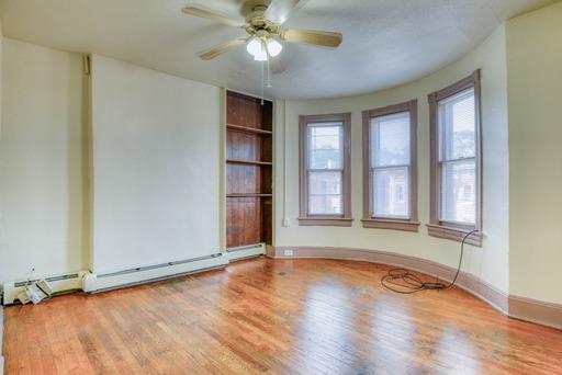unfurnished room with a healthy amount of sunlight, built in shelves, a ceiling fan, and wood finished floors