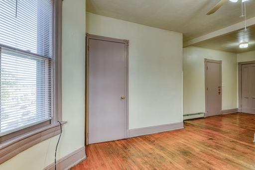 empty room with a ceiling fan, baseboard heating, wood finished floors, and a healthy amount of sunlight