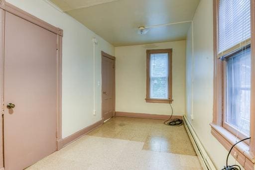 spare room featuring a baseboard heating unit, baseboards, and light floors