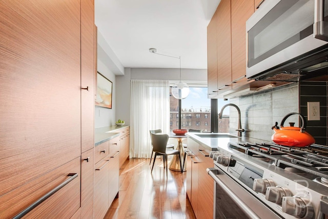 kitchen featuring light wood-style flooring, light countertops, decorative backsplash, stainless steel appliances, and a sink
