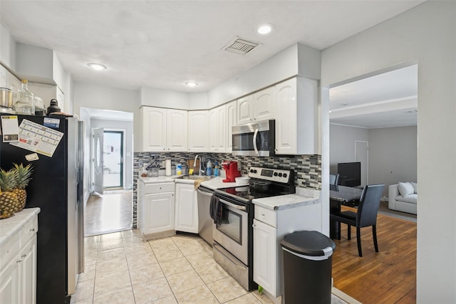 kitchen with white cabinets, stainless steel appliances, visible vents, decorative backsplash, and light countertops
