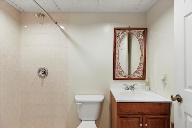 bathroom featuring toilet, vanity, a drop ceiling, and a tile shower