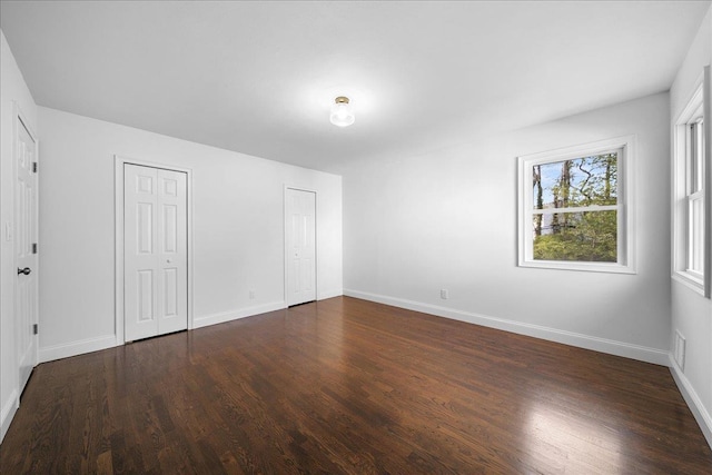 unfurnished bedroom with multiple closets, dark wood-style floors, and baseboards