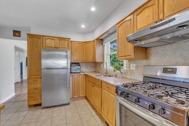 kitchen featuring tasteful backsplash, a sink, under cabinet range hood, light stone countertops, and stainless steel appliances