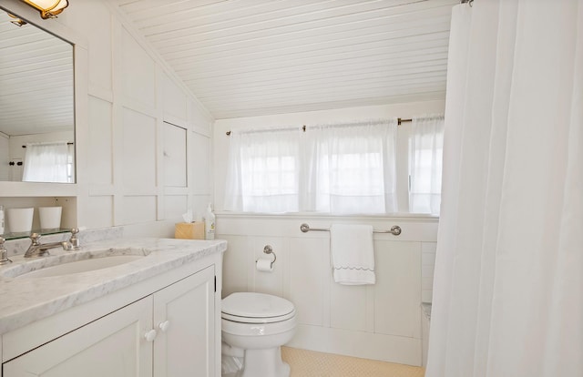 full bath featuring a decorative wall, vanity, toilet, and lofted ceiling