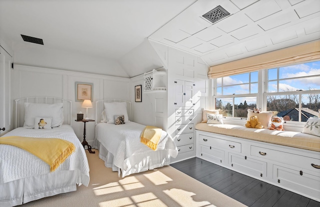 bedroom with dark wood-style floors, a decorative wall, visible vents, and lofted ceiling