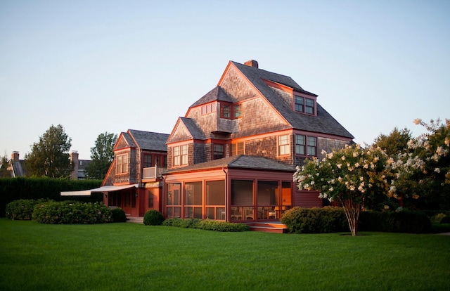 back of property with a sunroom, a chimney, and a lawn