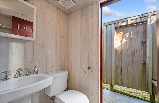 half bathroom with a sink, visible vents, toilet, and wooden walls