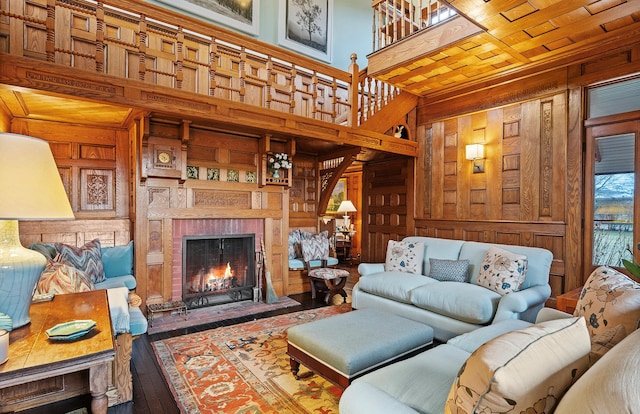 living room featuring built in features, a fireplace, a towering ceiling, hardwood / wood-style floors, and wooden walls