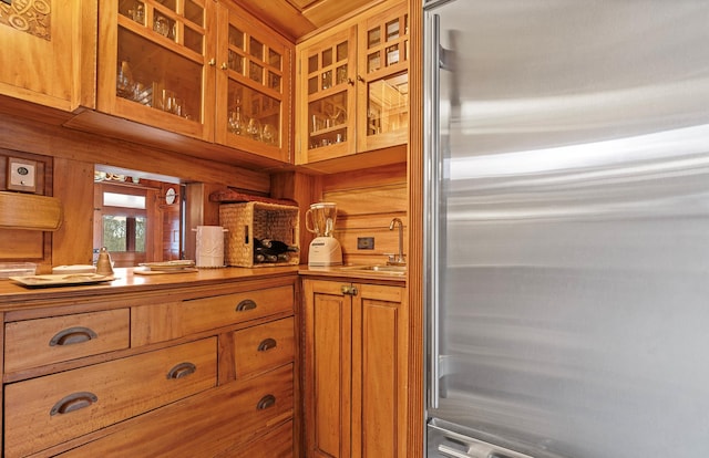 kitchen featuring glass insert cabinets, brown cabinetry, high quality fridge, a sink, and wooden walls