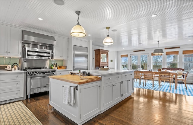 kitchen featuring butcher block countertops, wall chimney range hood, dark wood-style floors, a center island, and premium appliances