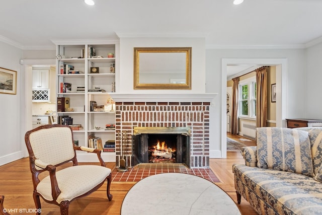 living room with radiator, wood finished floors, crown molding, a brick fireplace, and recessed lighting