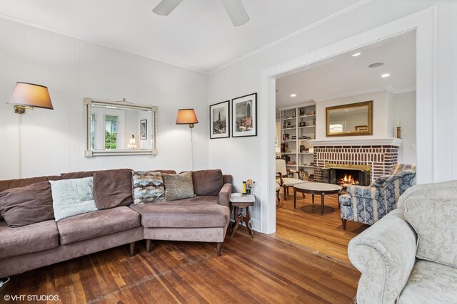 living area with wood finished floors, crown molding, a fireplace, a ceiling fan, and built in features