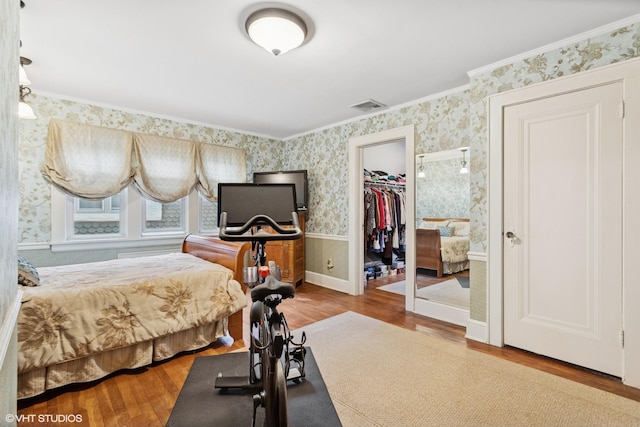 bedroom with wallpapered walls, wood finished floors, ornamental molding, a walk in closet, and a closet