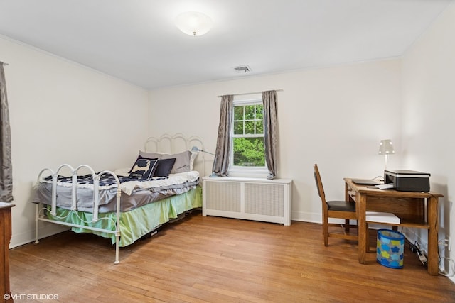 bedroom featuring radiator, crown molding, hardwood / wood-style flooring, baseboards, and an office area