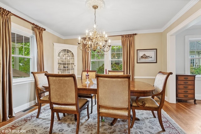 dining room with a chandelier, healthy amount of natural light, wood finished floors, and ornamental molding