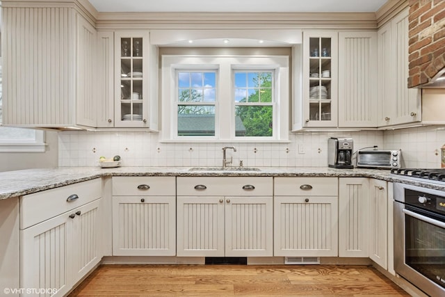 kitchen with oven, a sink, backsplash, gas stovetop, and light wood-type flooring