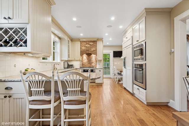 kitchen featuring appliances with stainless steel finishes, light stone counters, light wood-style flooring, backsplash, and a peninsula