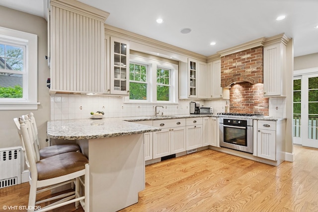 42 Hillcrest Ave, Larchmont, NY 10538 - kitchen with stainless steel appliances, a peninsula, radiator heating unit, light wood-type flooring, and glass insert cabinets