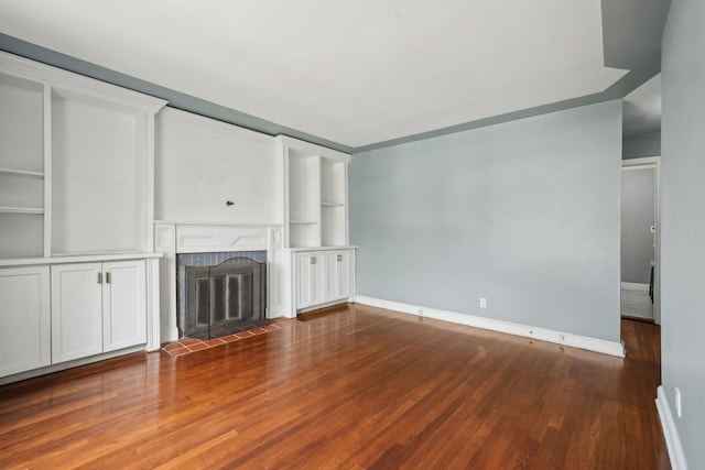 unfurnished living room with wood finished floors, a tiled fireplace, and baseboards