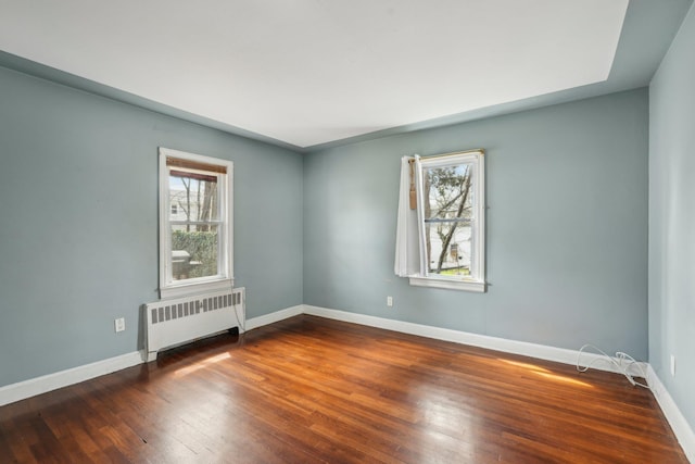 empty room with wood finished floors, radiator heating unit, and baseboards