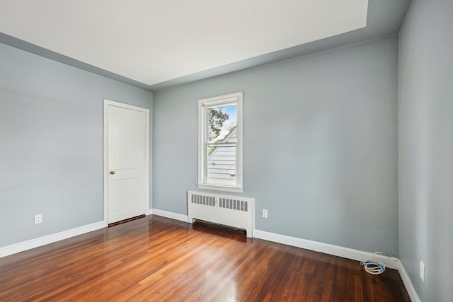 unfurnished room featuring radiator heating unit, baseboards, and wood finished floors
