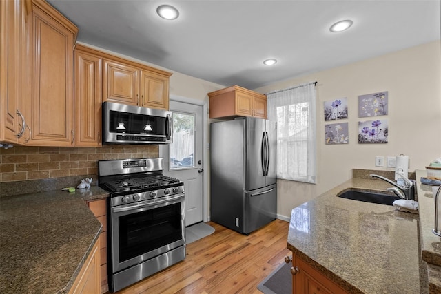 kitchen featuring stainless steel appliances, a sink, light wood-style floors, dark stone countertops, and recessed lighting