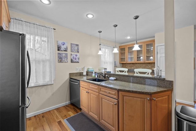 kitchen featuring stainless steel appliances, a sink, a peninsula, brown cabinets, and light wood finished floors