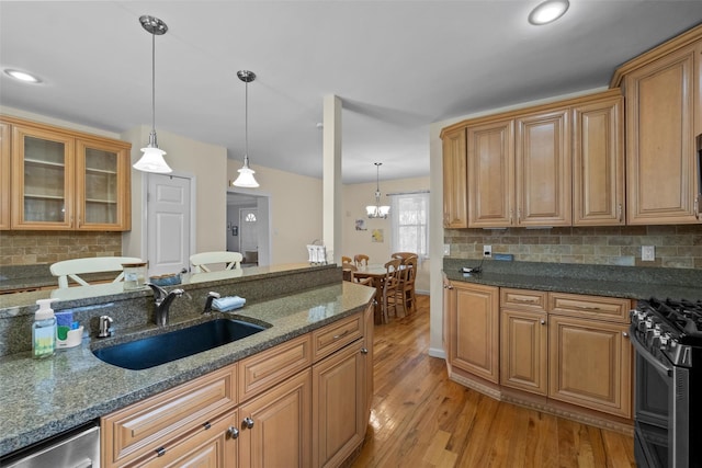 kitchen with stainless steel appliances, a sink, light wood-type flooring, tasteful backsplash, and hanging light fixtures